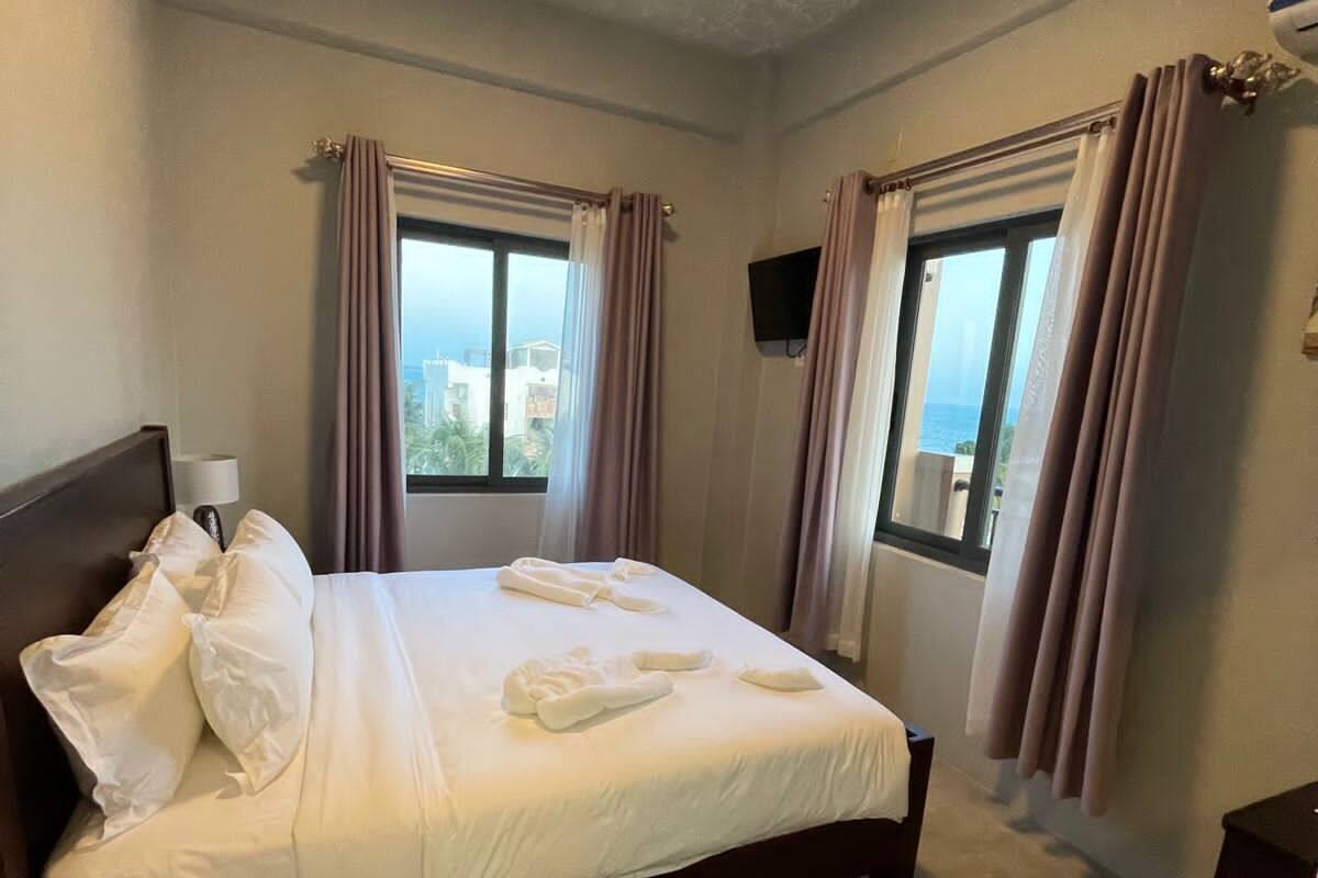 Ein Hotelzimmer mit Bett, Vorhängen, Fernseher und Meerblick.