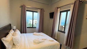 Une chambre d’hôtel avec un lit, des rideaux, une télévision et une vue sur la mer.