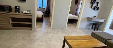 A spacious living area with a wooden coffee table, a sofa, and a bed in the background. There is a kitchenette with a microwave and coffee maker.