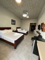 Una habitación de hotel con dos camas, un escritorio, una silla, un televisor y una lámpara de techo.