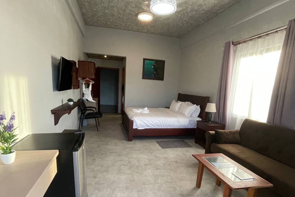 Ein Hotelzimmer mit Bett, Sofa, Schreibtisch, Fernseher und Deckenventilator.