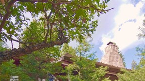 A red brick building with a white lattice fence, a staircase, and a tree in the foreground. - Cozy Cottage Cabin with Wood Burning Fireplace - Pet Friendly! Charming Updates! (Cloudcroft)