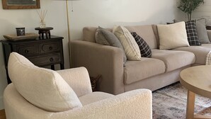 A living room with a beige sofa, a round coffee table, a floor lamp, and a small side table with decorative items. - Cozy Cottage Cabin with Wood Burning Fireplace - Pet Friendly! Charming Updates! (Cloudcroft)