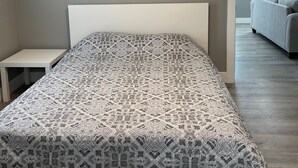 Makuuhuoneessa on sänky, yöpöytä, kattotuuletin ja näkymä toiseen huoneeseen.