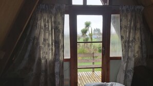 A bedroom with a bed, a wooden floor, and a view of a garden through a glass door.