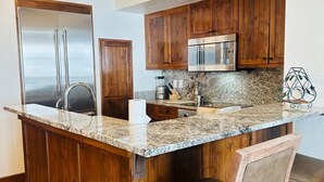 Eine Küche mit Holzausstattung, einem Edelstahlkühlschrank, einer Mikrowelle und einer Arbeitsplatte aus Granit.