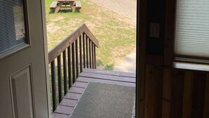 Vista da una stanza su una terrazza con ringhiera in legno e tavolo da picnic, affacciata su un'area verde e uno specchio d'acqua.