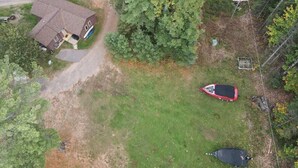 Vista aerea di una zona residenziale con una casa, un'auto rossa e un veicolo nero parcheggiati su un prato.