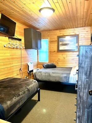 Cozy cabin-style room with two single beds, a table, and a chair, featuring a window with a view of the sky.