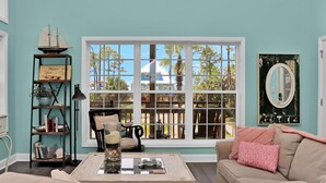 A cozy living room with a large window, a bookshelf, a lamp, and a sofa. - Rehoboth Cottage (Port St. Joe)