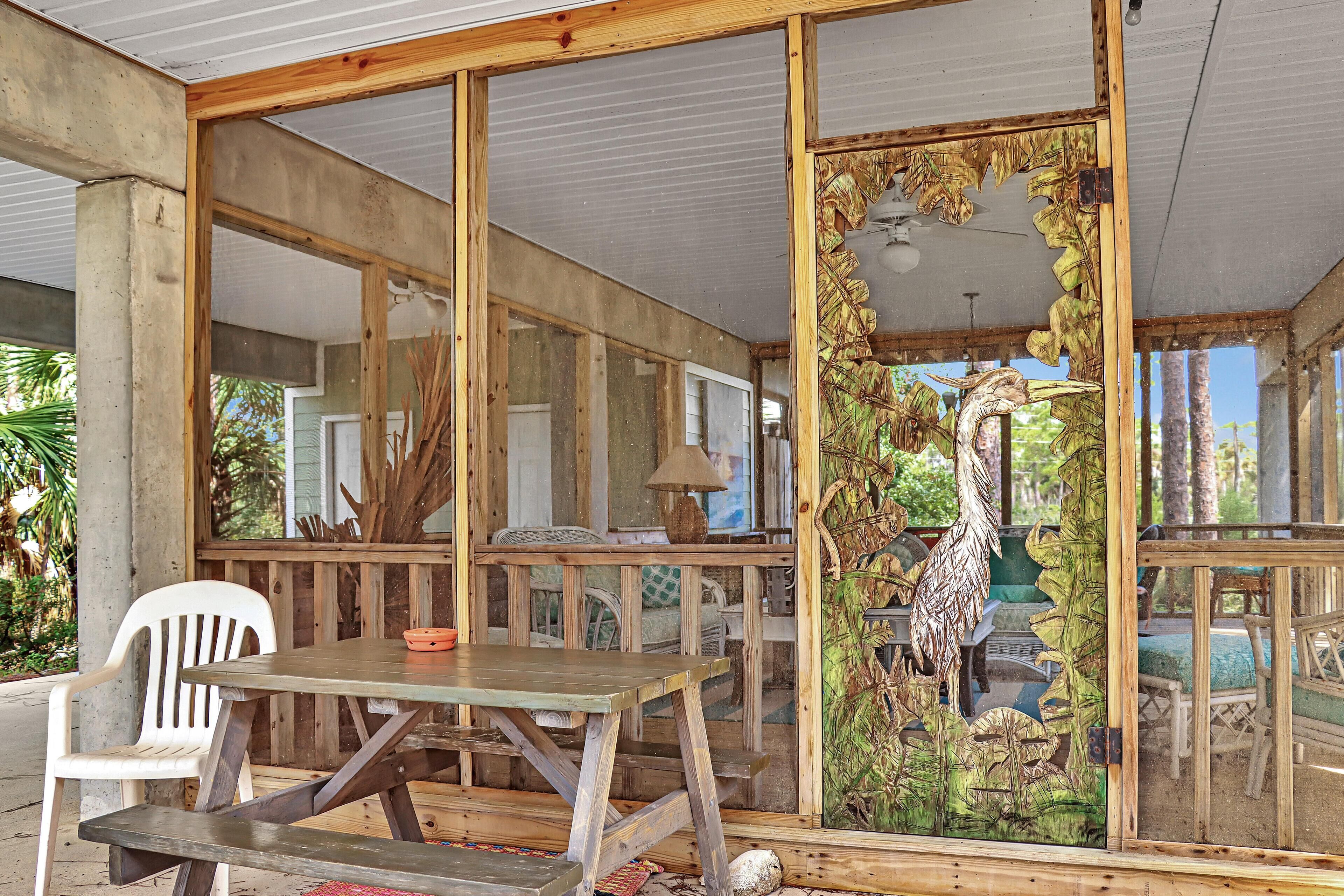A wooden deck with a table and chairs, a decorative wooden panel with a bird design, and a view of the outdoors.