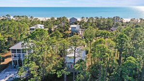 A coastal property with multiple houses surrounded by dense pine trees, a beach in the background, and a clear view of the ocean. - Rehoboth Cottage (Port St. Joe)