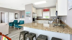 A modern kitchen with white cabinets, a granite countertop, and a 'SEAFOOD' sign. - Pearly Shells (Port St. Joe)