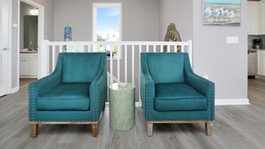 A room with teal upholstered chairs, a small round side table, and a view of the outdoors through a window. - Pearly Shells (Port St. Joe)