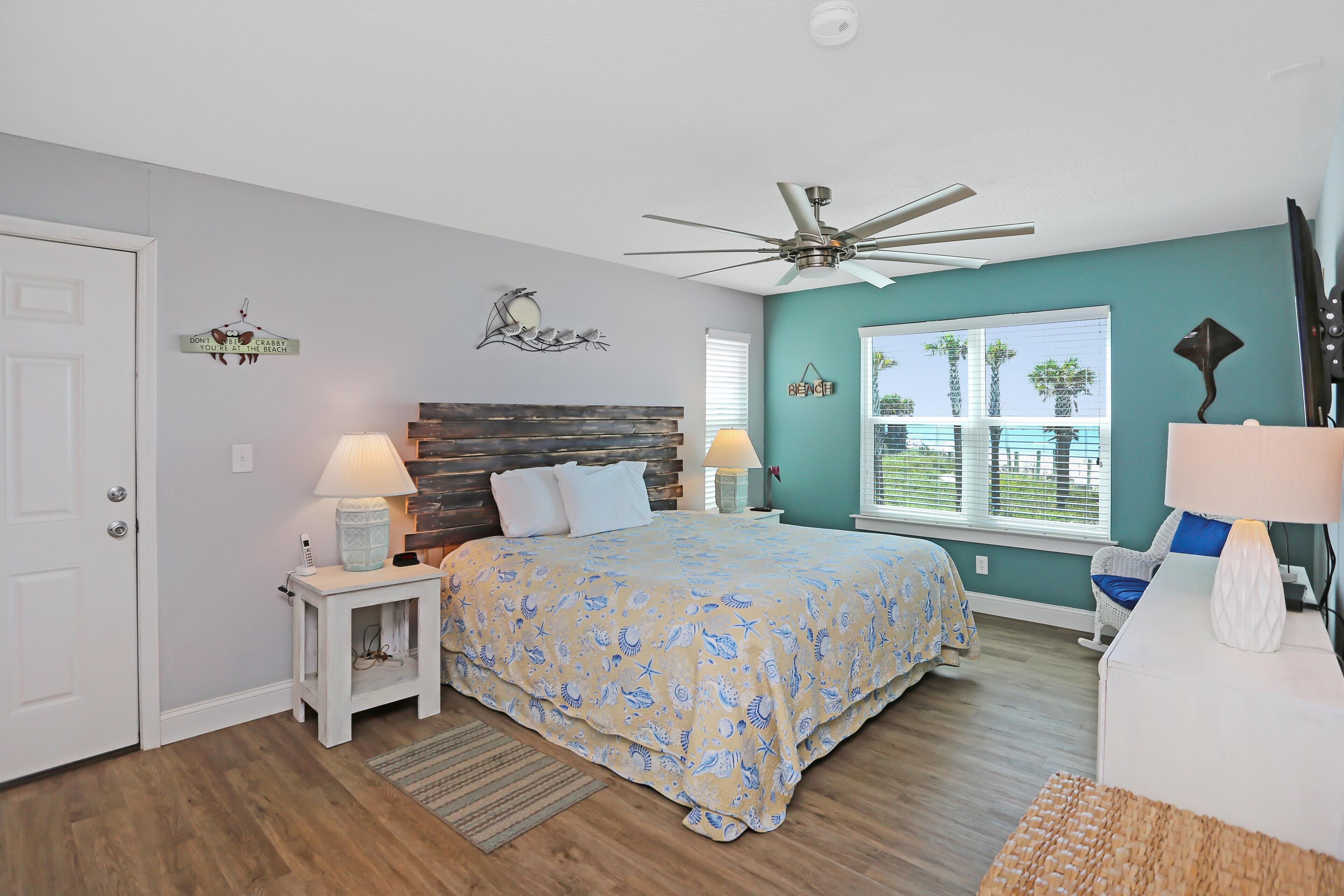A bedroom with a bed, two bedside tables, a ceiling fan, a window with blinds, and a door.