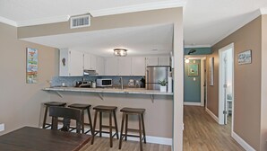 A kitchen with a central island, bar stools, and a dining table. - Paradise By The Gulf (Port St. Joe)