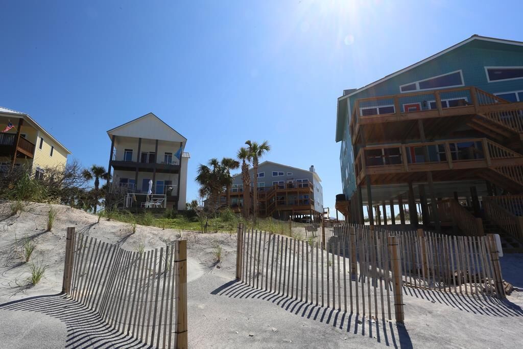 A beachfront property with multiple buildings, including a two-story house with a balcony and a larger building with a wooden deck.
