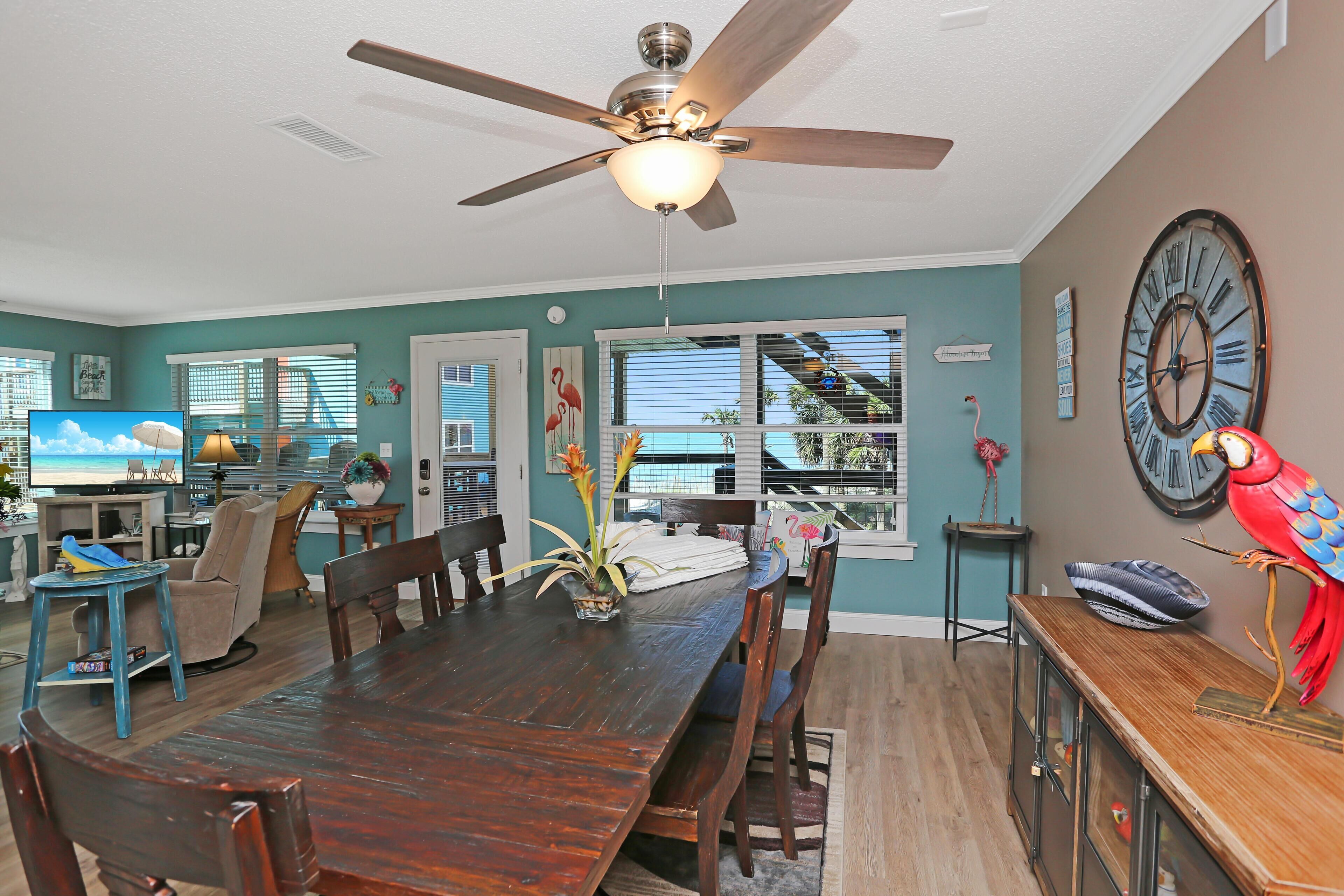 A dining area with a wooden table, chairs, a ceiling fan, and a large wall clock.