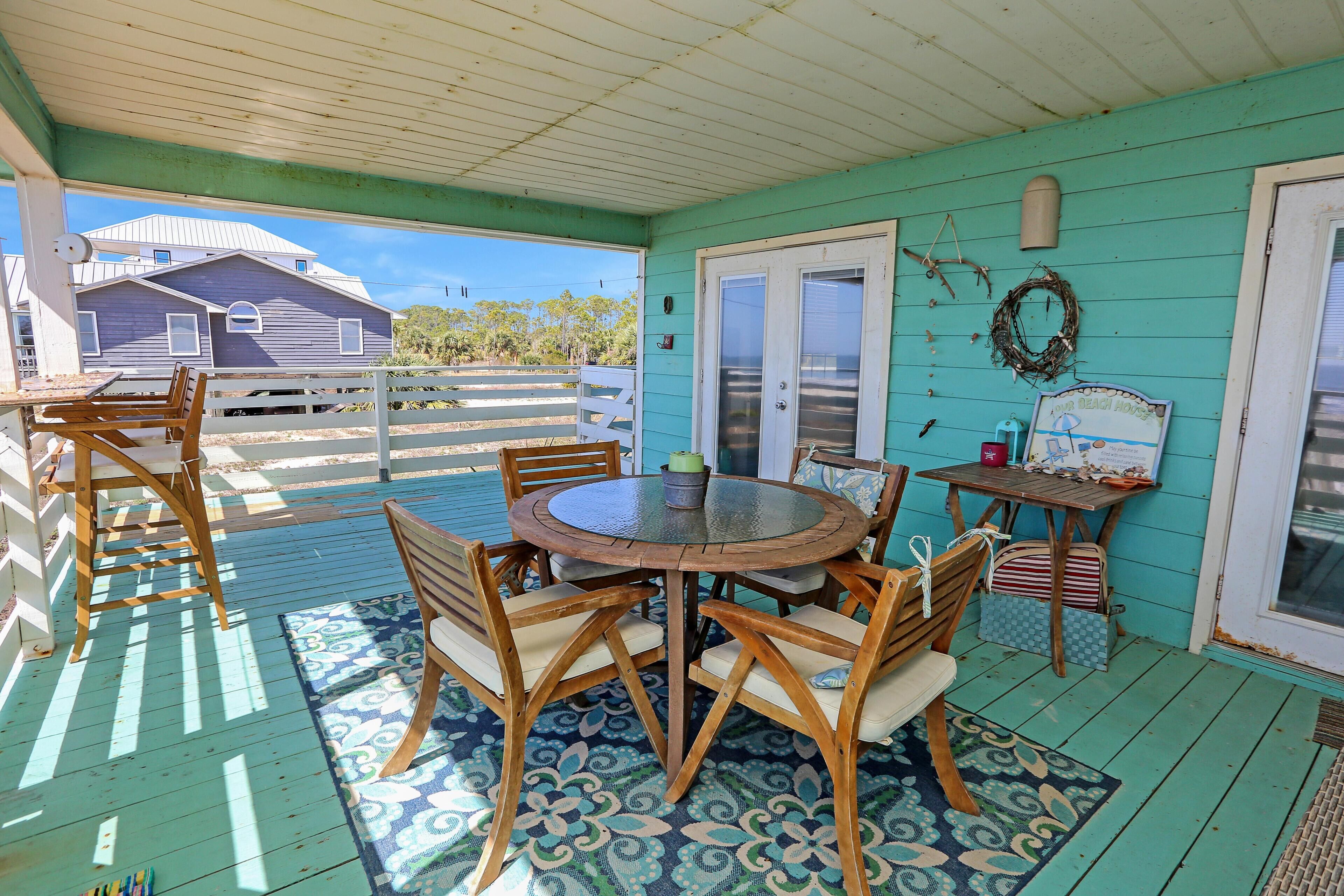A covered outdoor area with a wooden table and chairs, a patterned rug, and a door with a wreath.