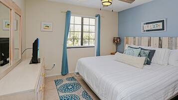 A bedroom with a bed, a TV, a window with curtains, a ceiling fan, and a rug.