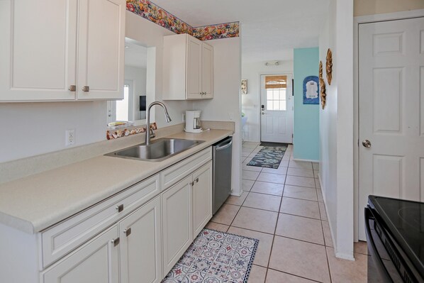 A kitchen with white cabinets, a stainless steel sink, and a coffee maker. - Pelican Bend (Port St. Joe)