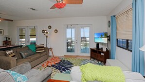 A living room with a sofa, a coffee table, a TV, and a view of the outdoors through a sliding door. - Pelican Bend (Port St. Joe)