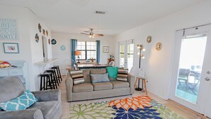 A living room with a sofa, a coffee table, and a dining area with a table and chairs. There is a door leading to an outdoor area. - Pelican Bend (Port St. Joe)