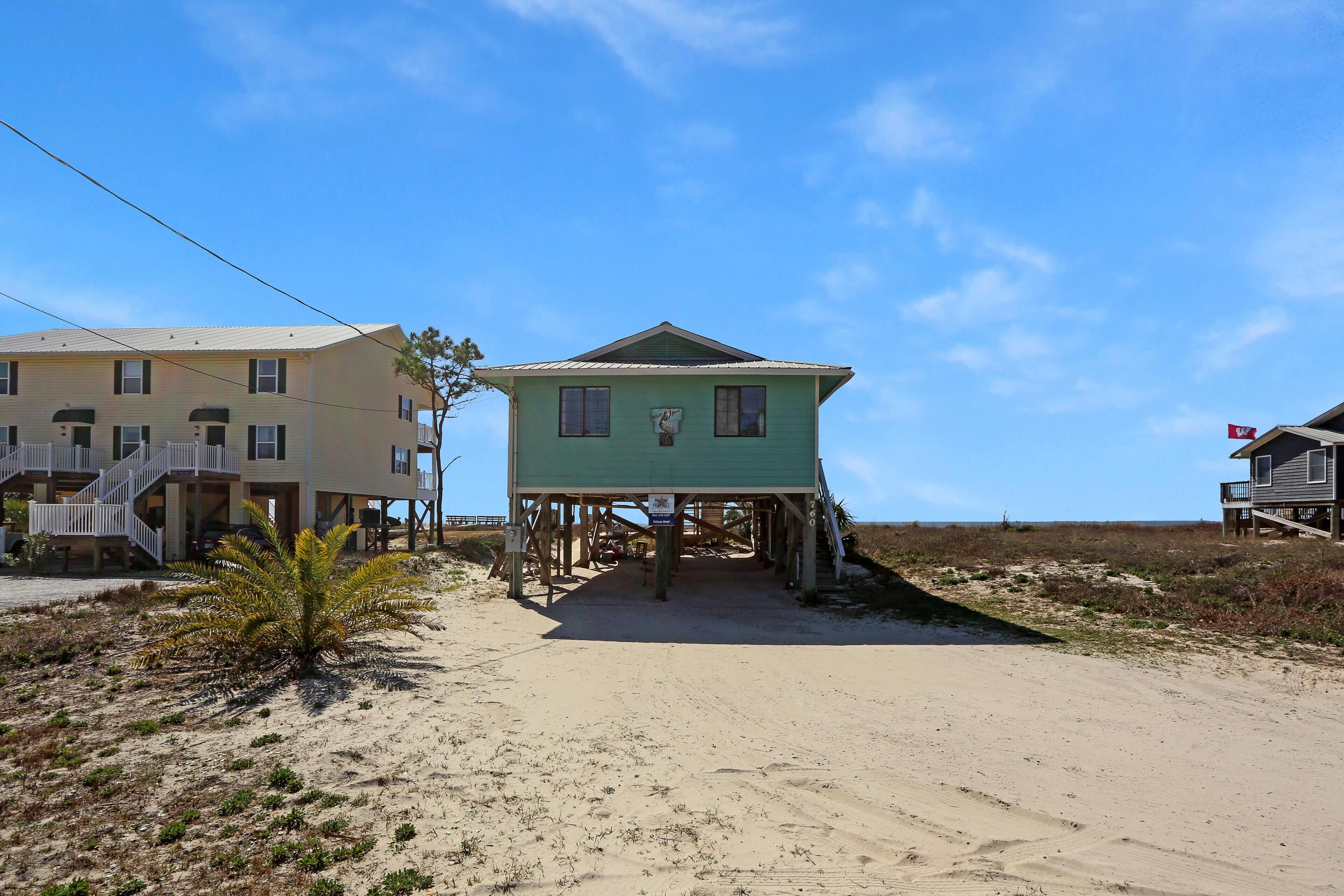A beachfront house with a wooden deck and a small staircase leading to the entrance.