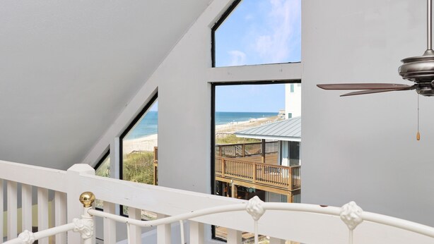 Een balkon met uitzicht op het strand, een plafondventilator en een witte reling.