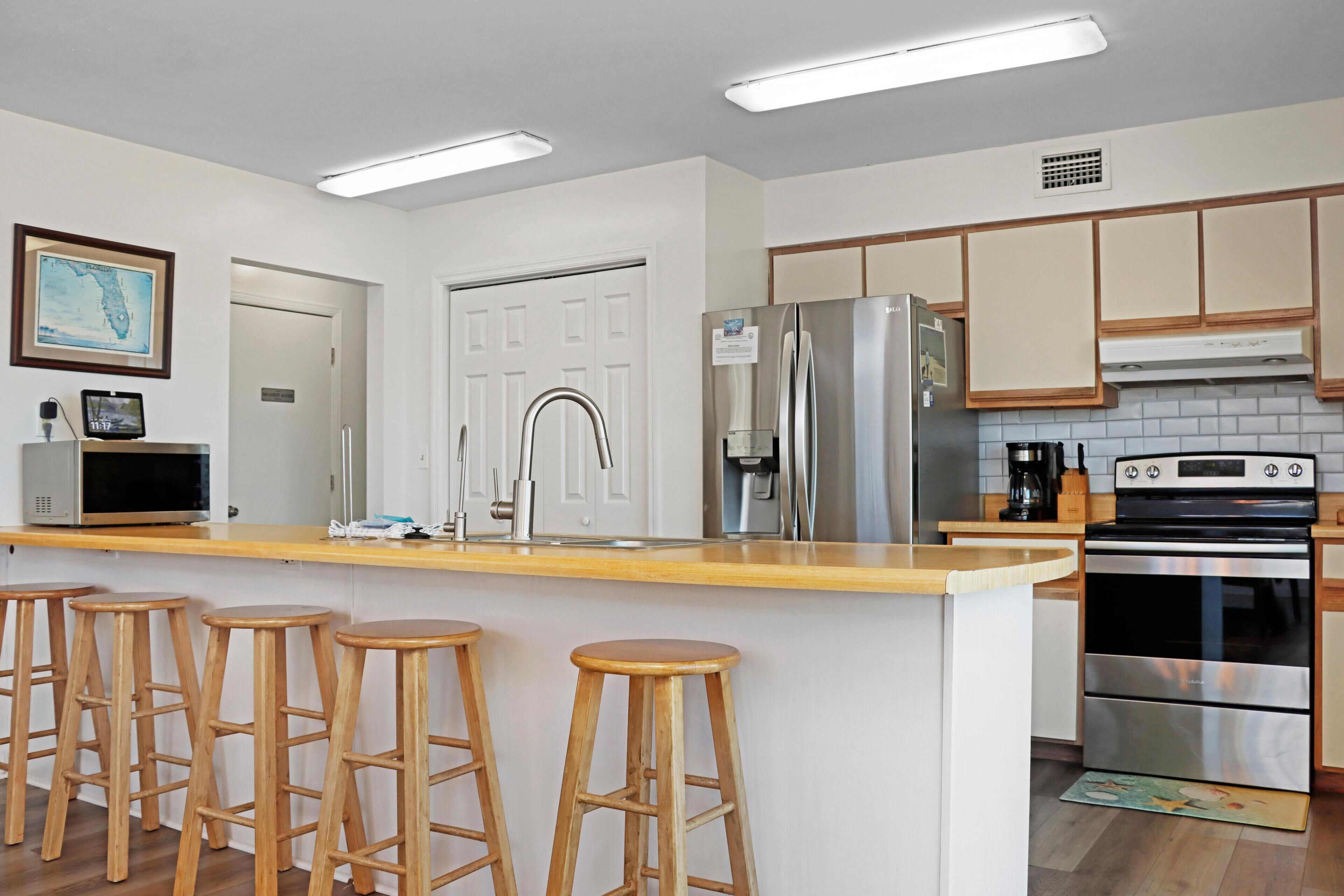 A modern kitchen with a central island, bar stools, stainless steel appliances, and wooden cabinets.