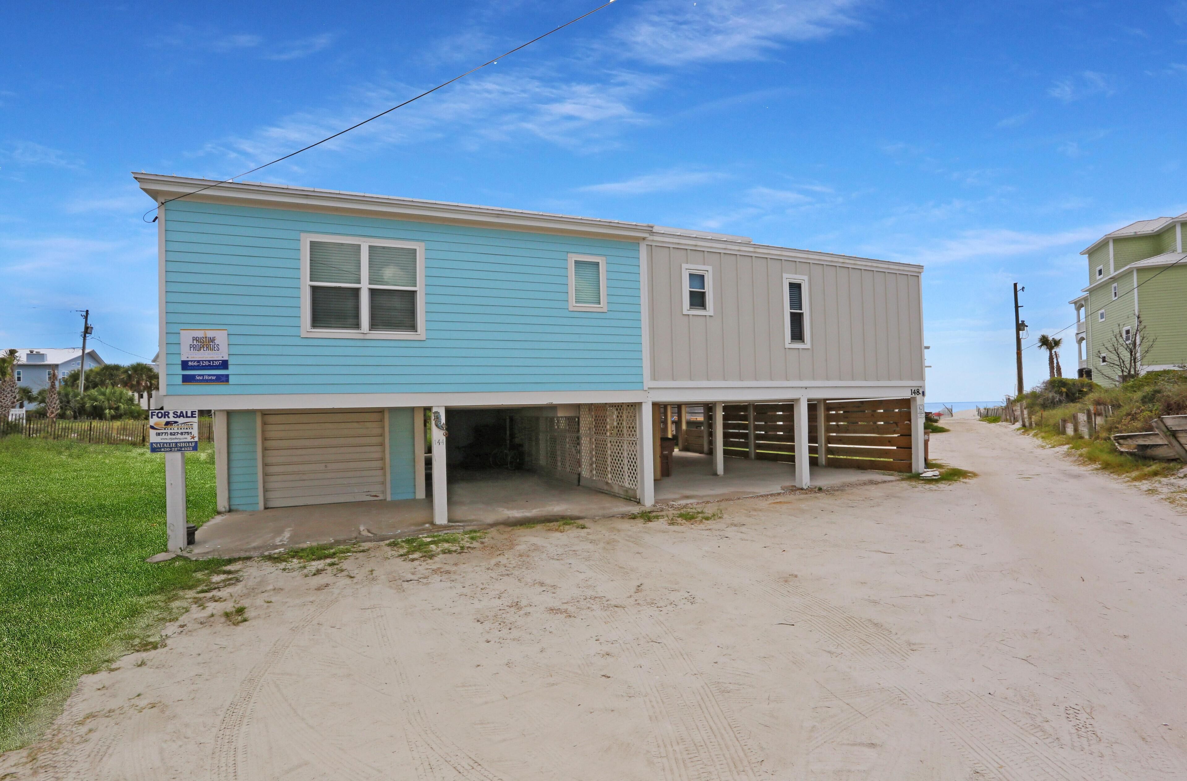 A two-story house with a garage, a covered porch, and a sandy driveway.