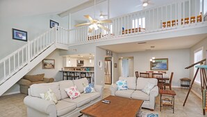 A spacious living area with a high ceiling, a staircase, and a balcony. - Sharkey's (Port St. Joe)