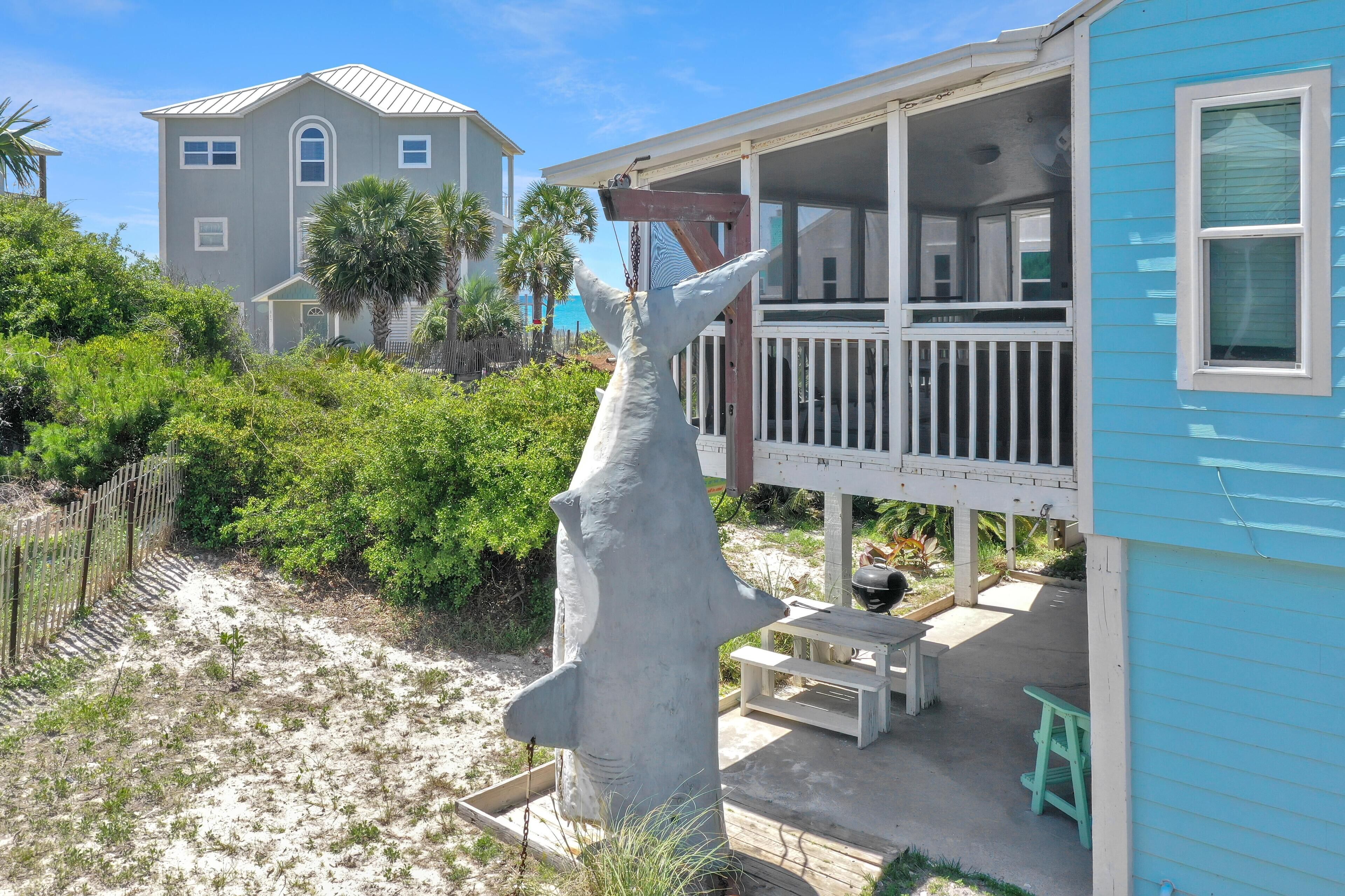 A beachfront property with a large white sculpture, a covered porch, and a house in the background.