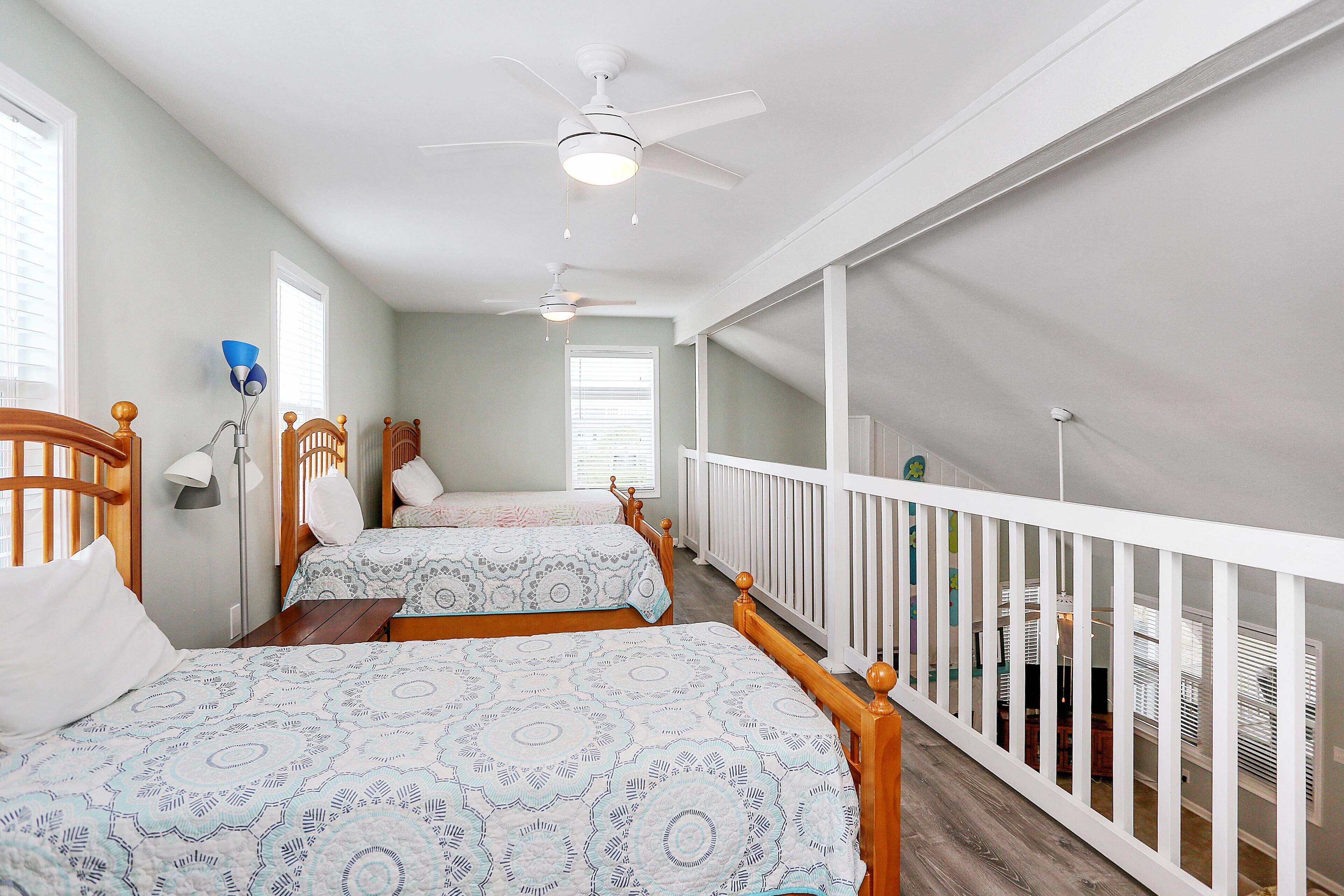 Une chambre avec deux lits, un ventilateur de plafond et une balustrade blanche.