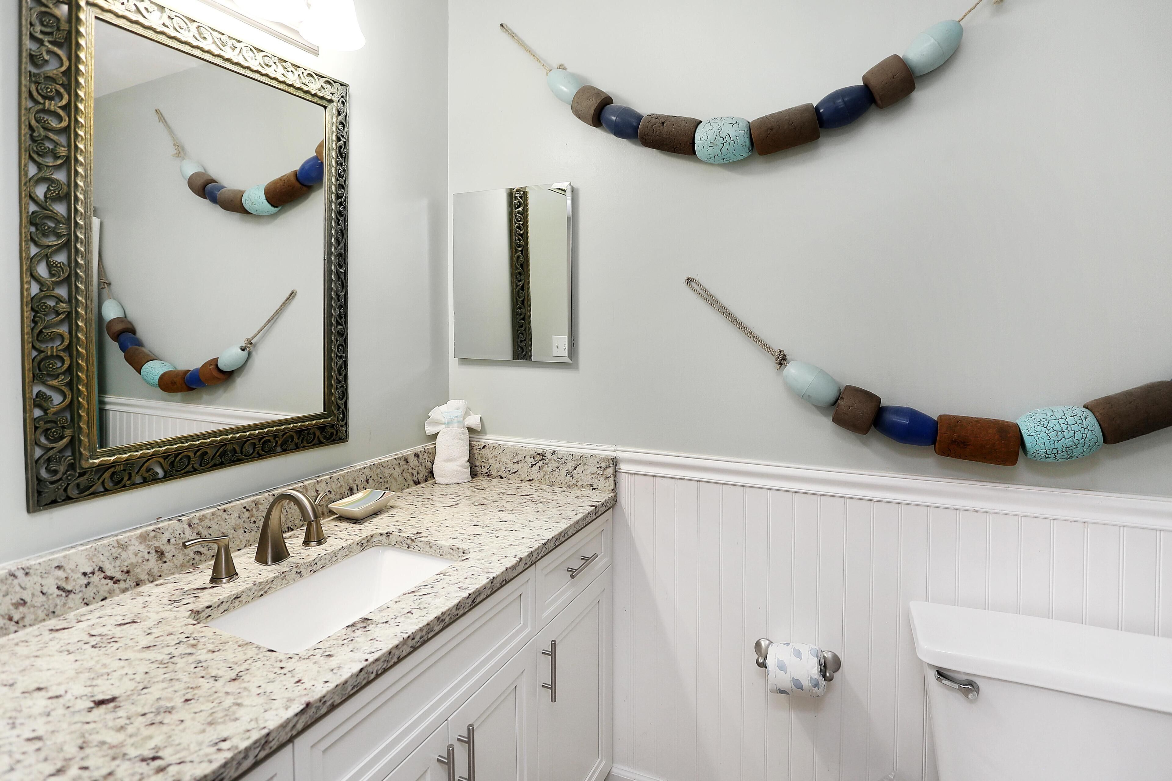 Un bagno con lavabo su piano in granito, uno specchio con cornice decorata e collane di perle ornamentali appese al muro.