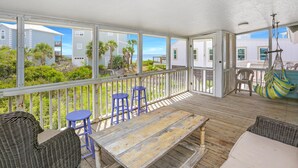 A covered outdoor area with a wooden deck, wicker furniture, and a view of the ocean and neighboring buildings. - Sharkey's (Port St. Joe)