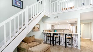 A spacious living area with a staircase, a kitchen with bar stools, and a beige sofa. - Sharkey's (Port St. Joe)
