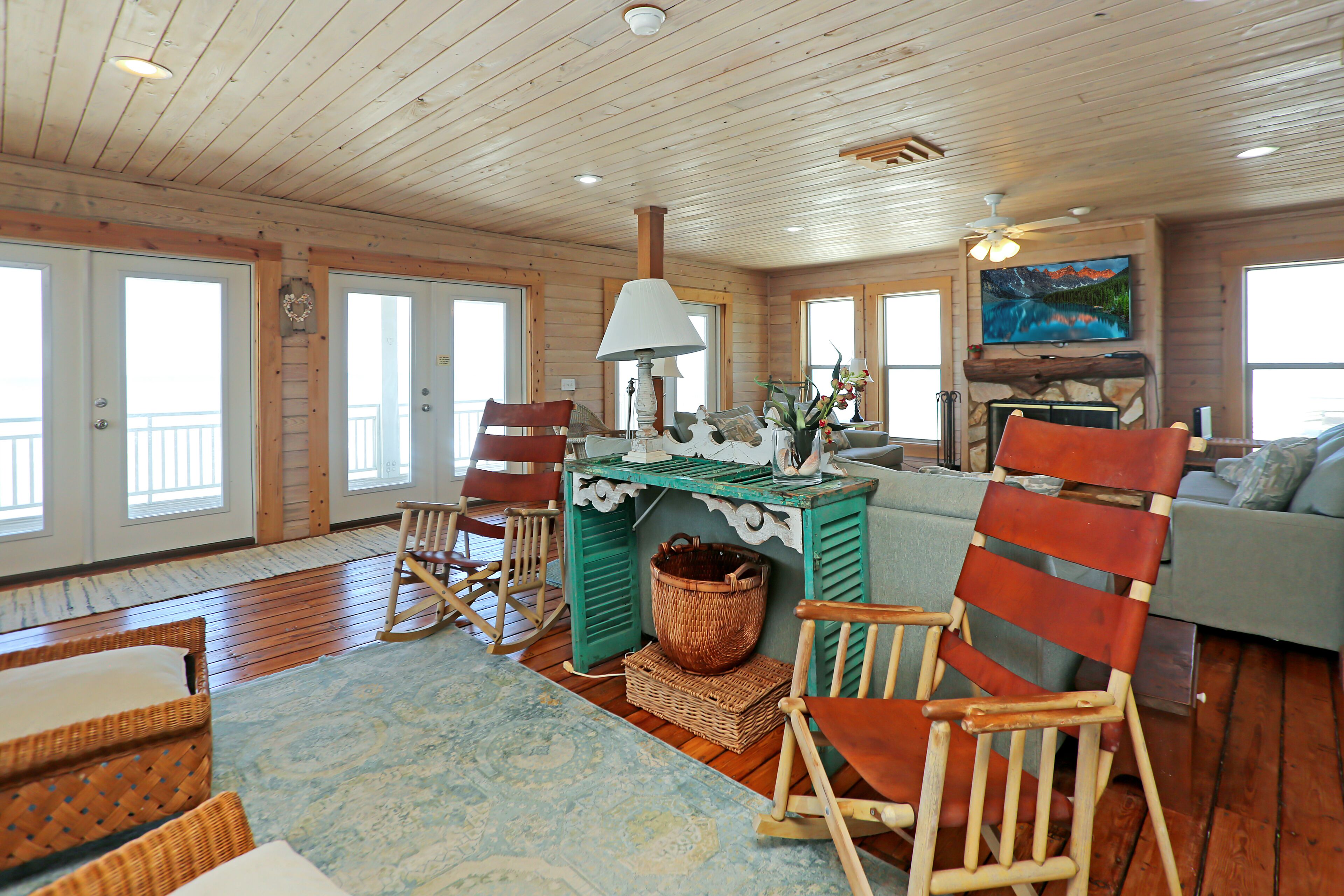 A spacious living room with wooden floors, a blue patterned rug, a green table, and a large painting on the wall.