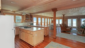 Una cocina amplia con armarios de madera, una isla central y un refrigerador. Amplias ventanas ofrecen luz natural y vistas.