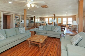 A spacious living room with a wooden floor, a large grey sectional sofa, a wooden coffee table, and a dining area with a table and chairs. - Ramblin Wreck (Port St. Joe)