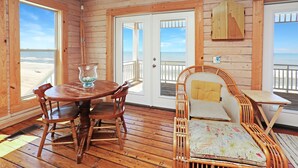 Una cabaña de madera con una mesa y sillas, un sofá de mimbre y vista a la playa a través de las puertas.