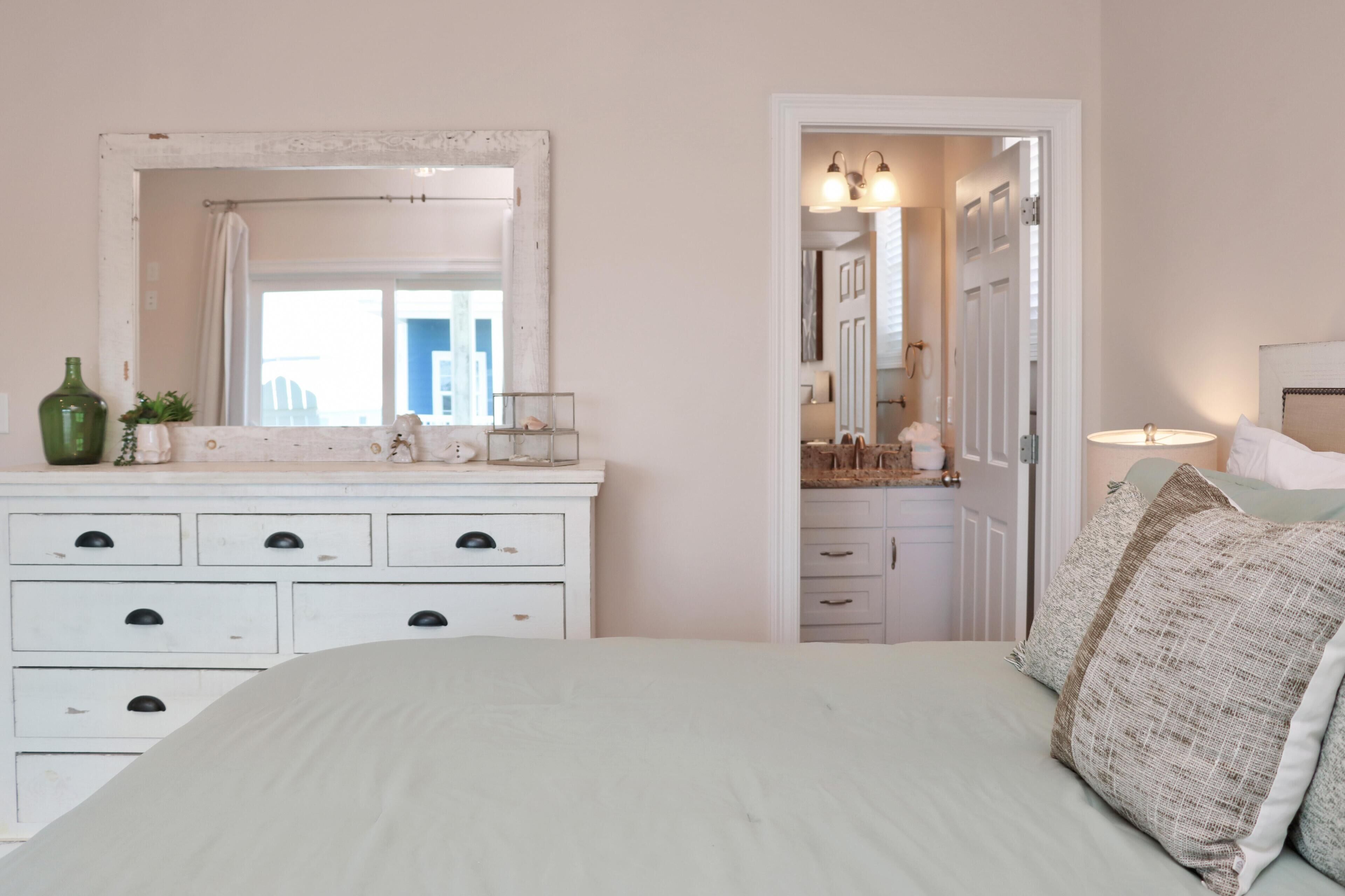 A bedroom with a bed, a dresser, a mirror, and a door leading to a bathroom.