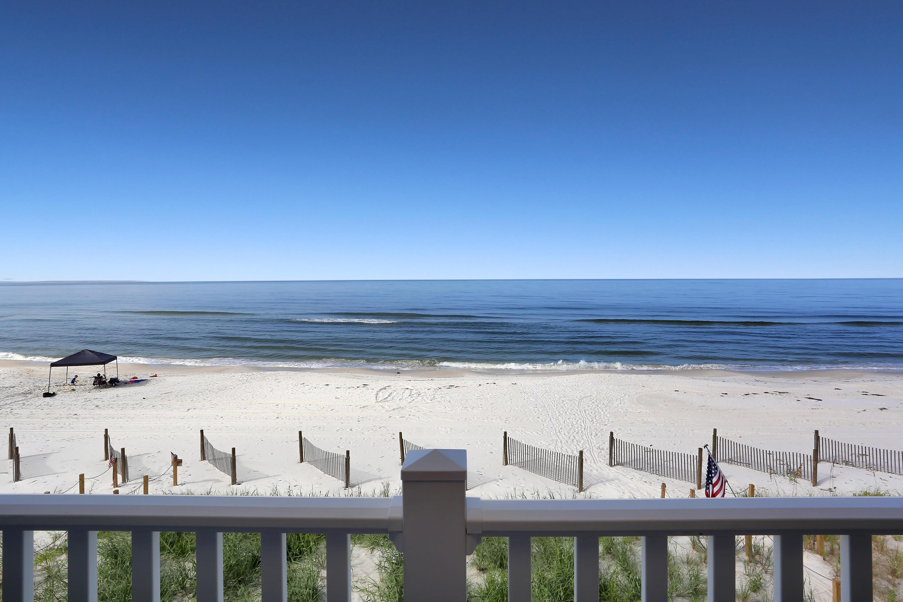 A beach with a wooden fence, a small American flag, and a clear blue sky.