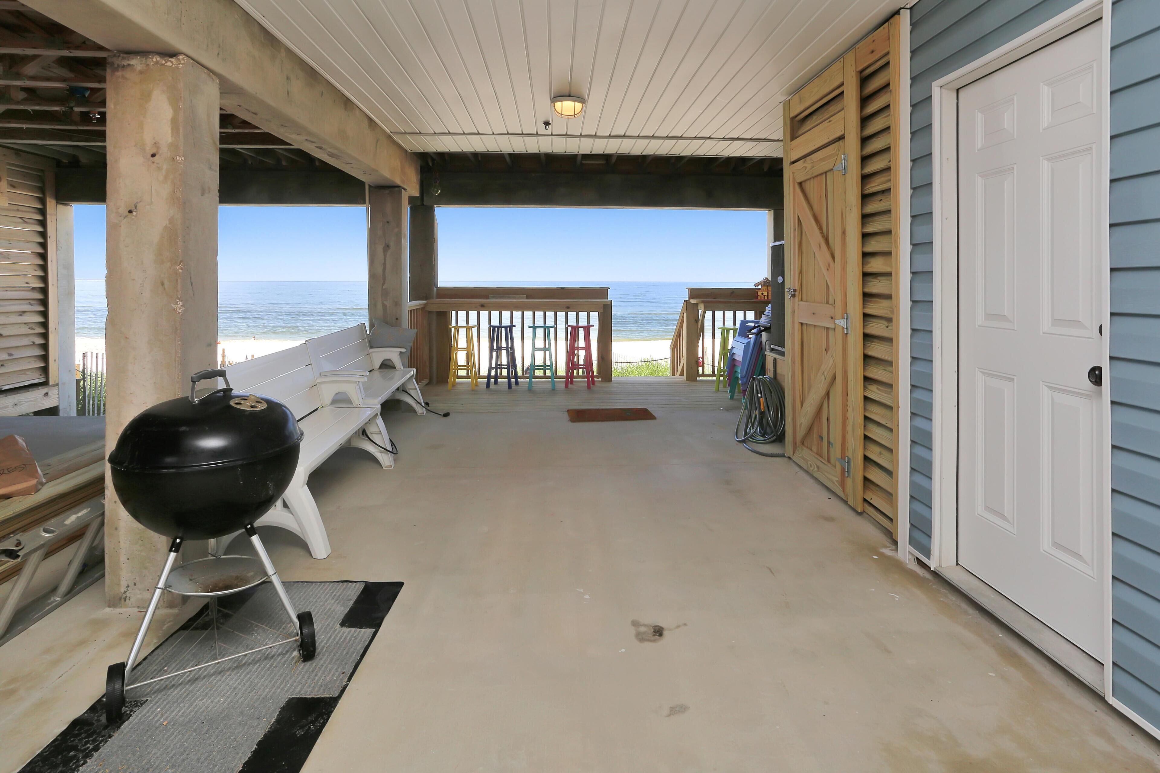 A covered outdoor area with a grill, benches, and a view of the beach.