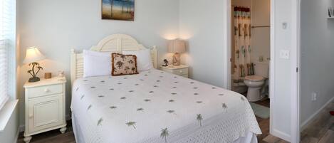 A bedroom with a bed, nightstands, a ceiling fan, a painting, and a bathroom visible through an open door.