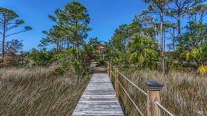 A wooden boardwalk leading to a building surrounded by tall trees and grassy areas. - Hideaway Bay (Port St. Joe)