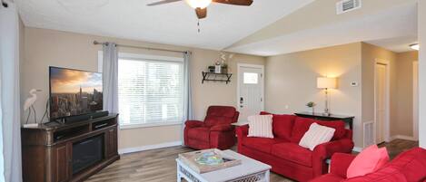 A living room with a ceiling fan, a red sofa, a coffee table, and a television.
