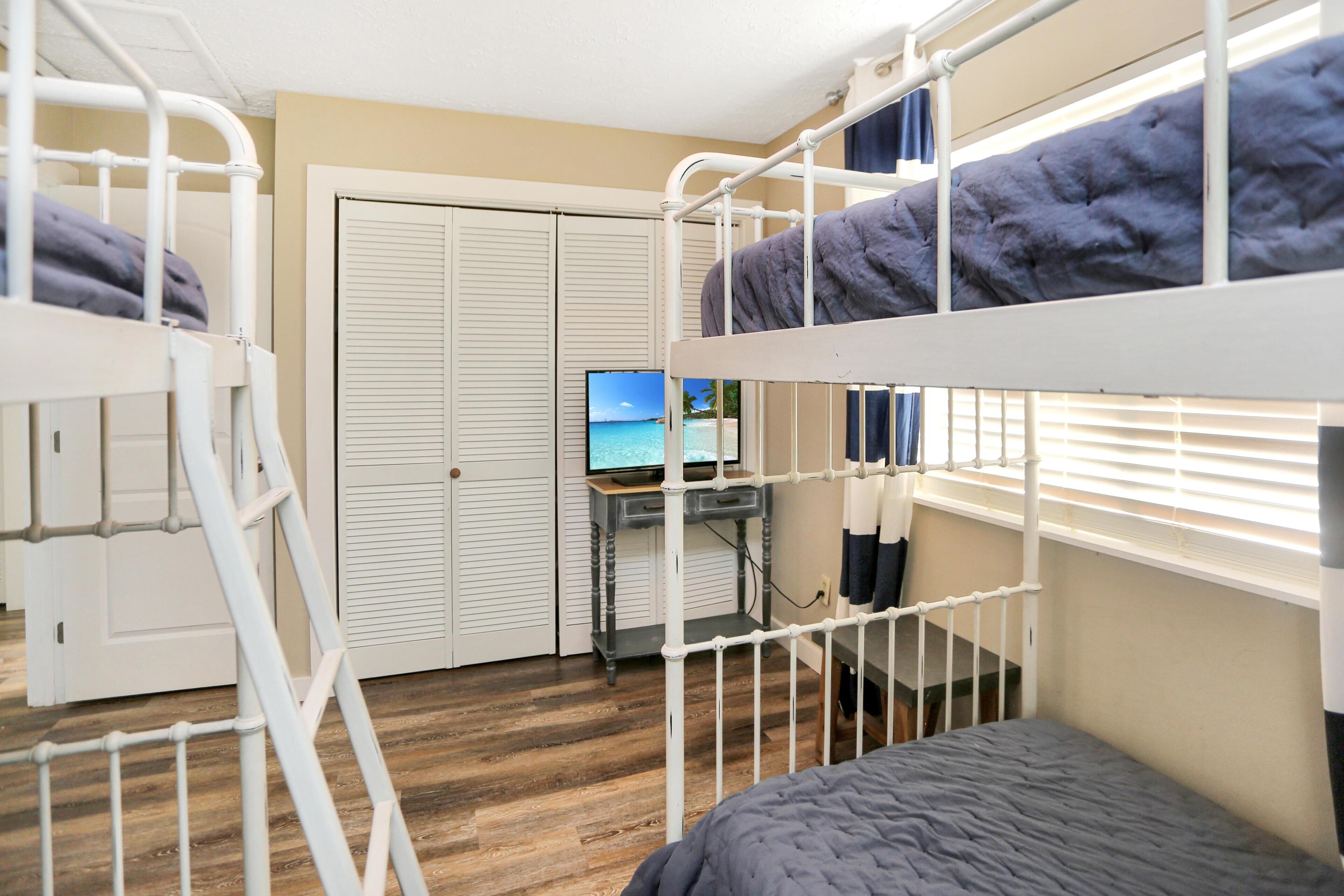 A bunk bed room with a desk and computer, a door, and a window with blinds.