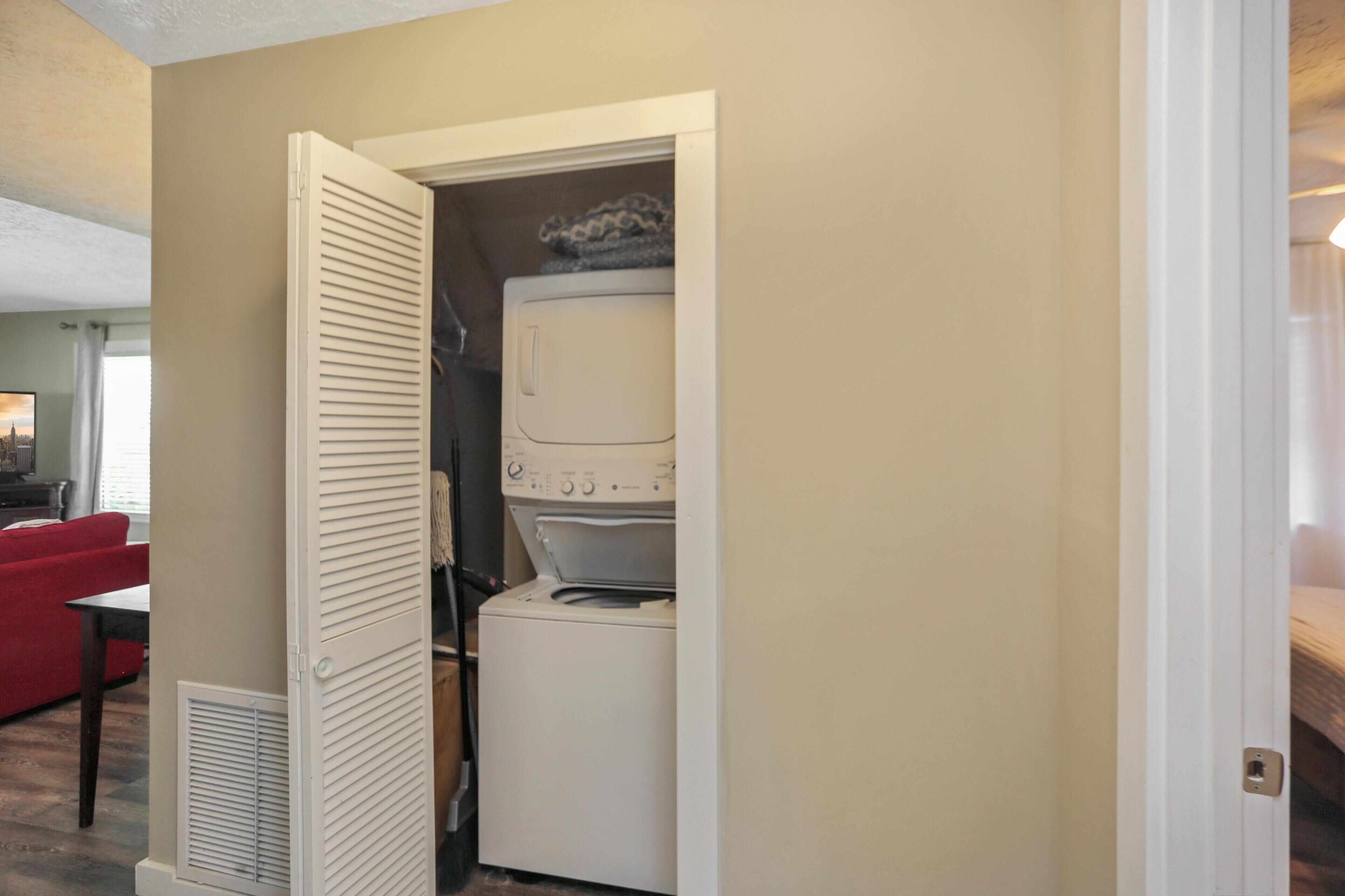 A laundry room with a washing machine and dryer, a red couch, and a vent.