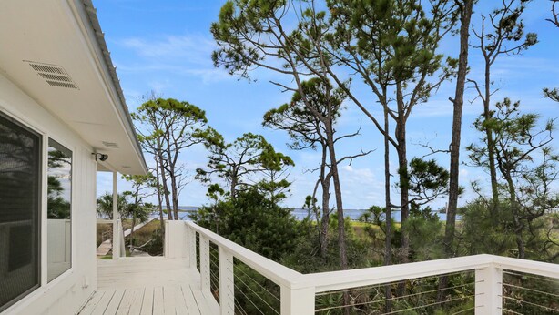 A wooden deck with a white railing overlooking a natural landscape with trees and a body of water. - Hideaway Bay (Port St. Joe)